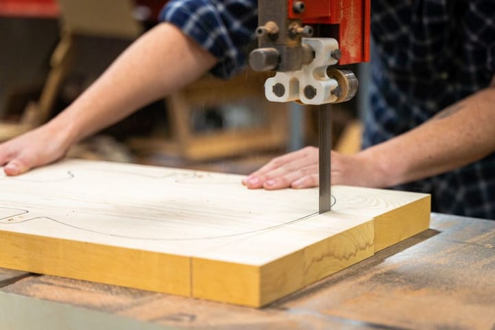 woman cuts a guitar body out of a spread of wood on a bandsaw.